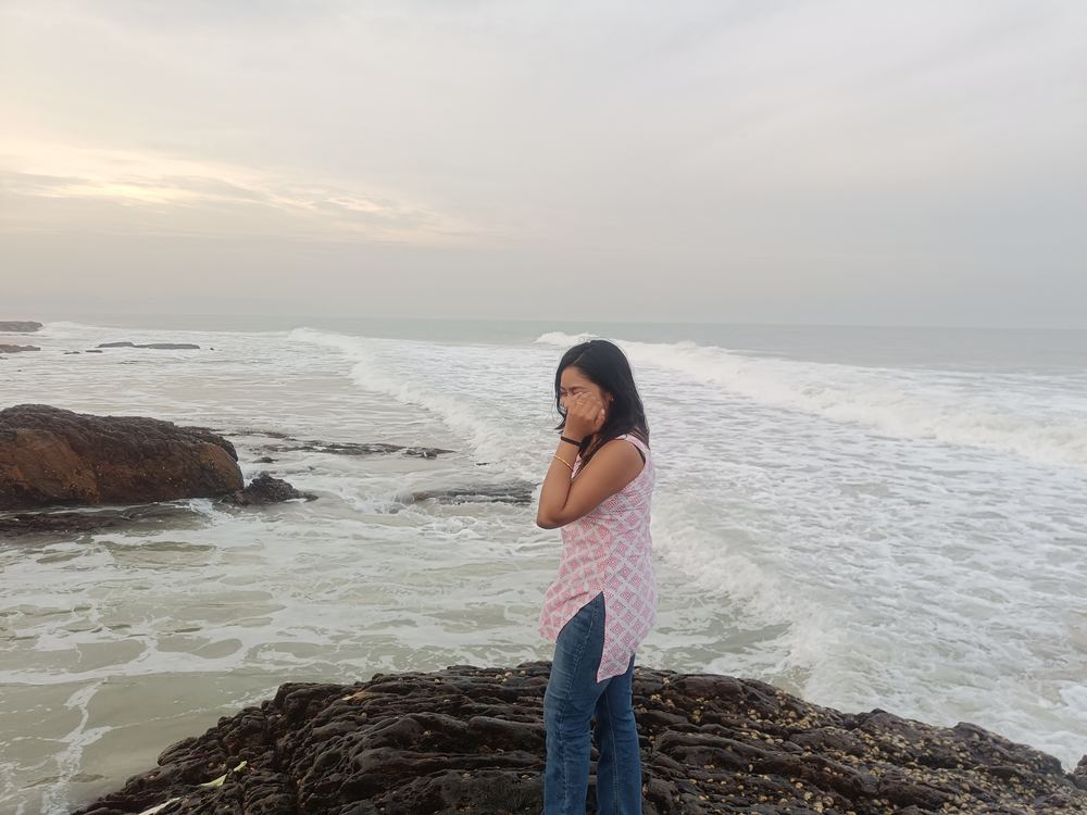 Shruti laughing with her hand near her face by the sea